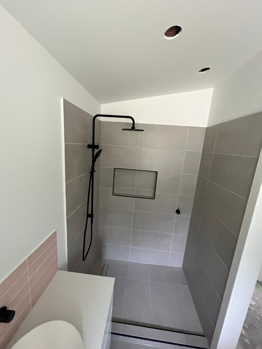 Shower recess tiled in large-format grey tiles with recessed niche and matte black rail shower — Cranbourne South by Casey Quality Coatings