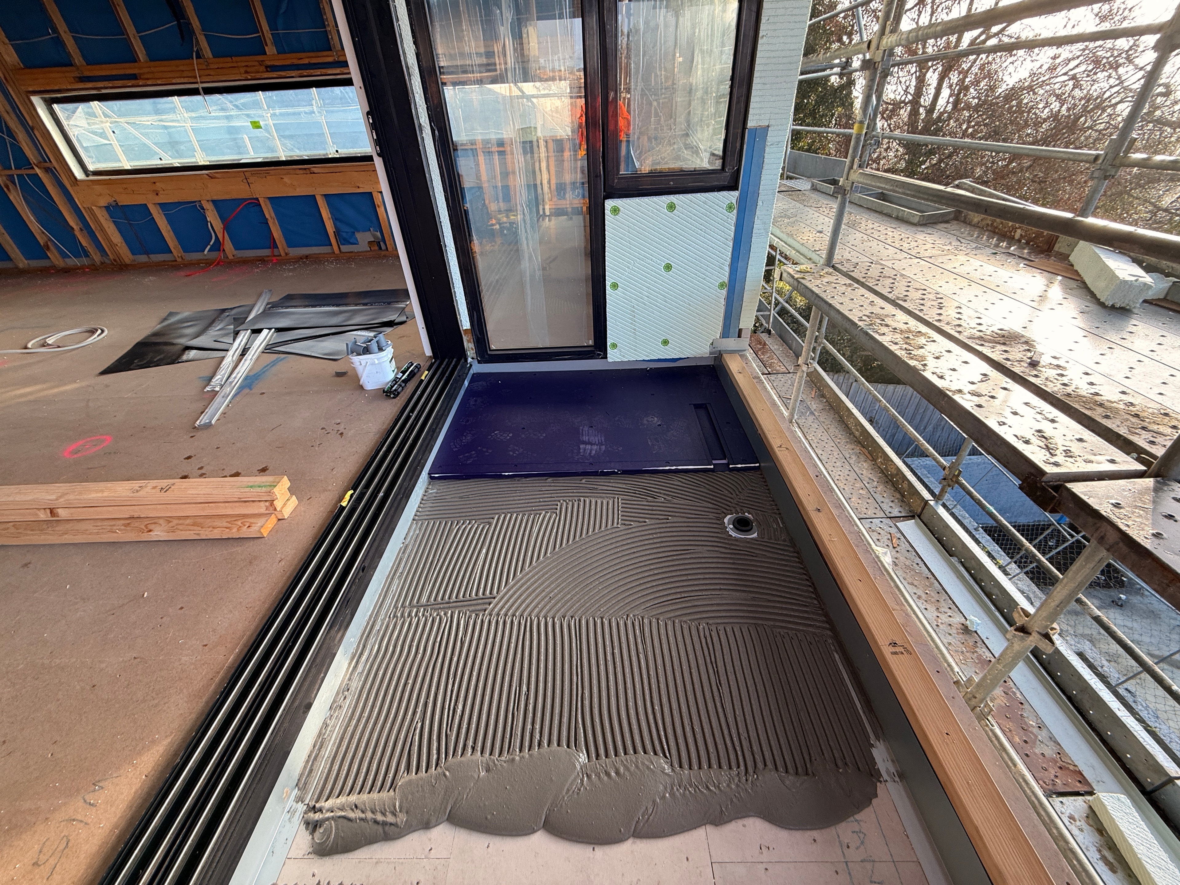 Overhead view of full balcony deck with purple waterproofing membrane fully applied, two tradies in hi-vis on site — Dandenong new-build by Casey Quality Coatings