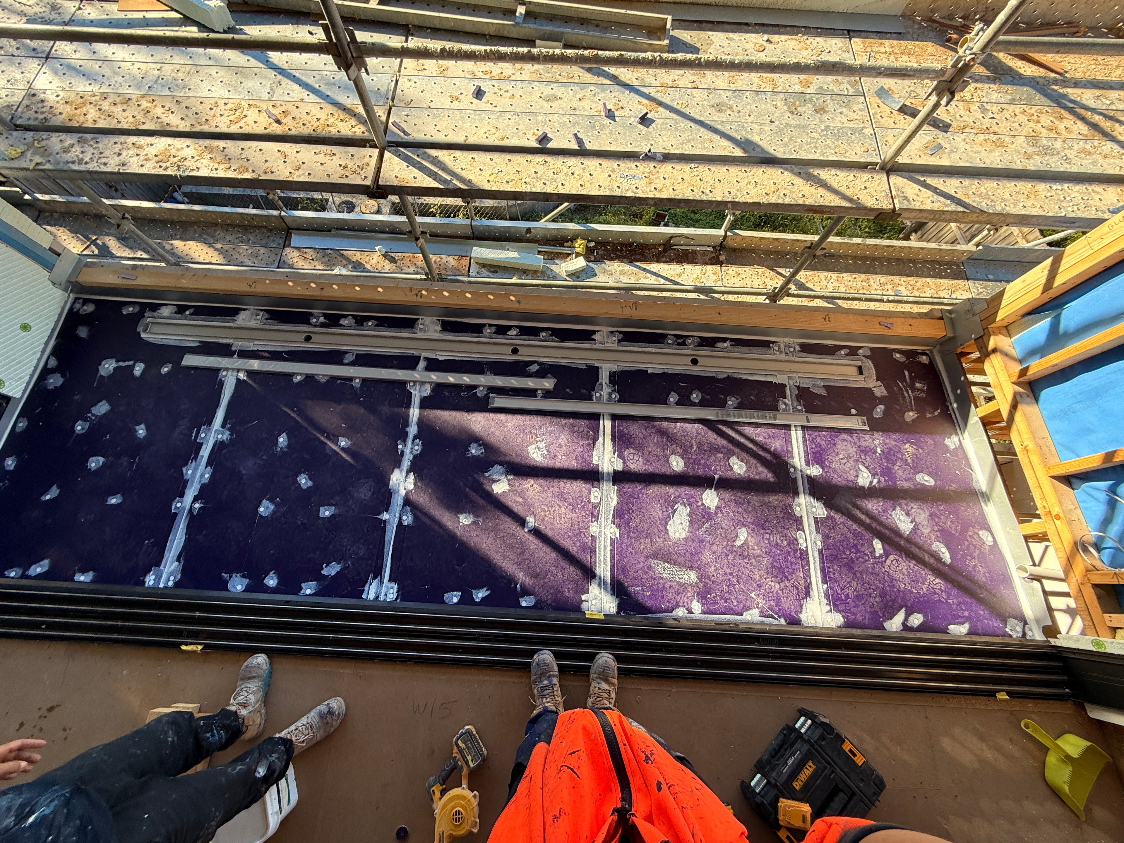 Overhead view of balcony membrane with aluminium door threshold track being installed over purple waterproofing membrane, two tradies working — Dandenong by Casey Quality Coatings