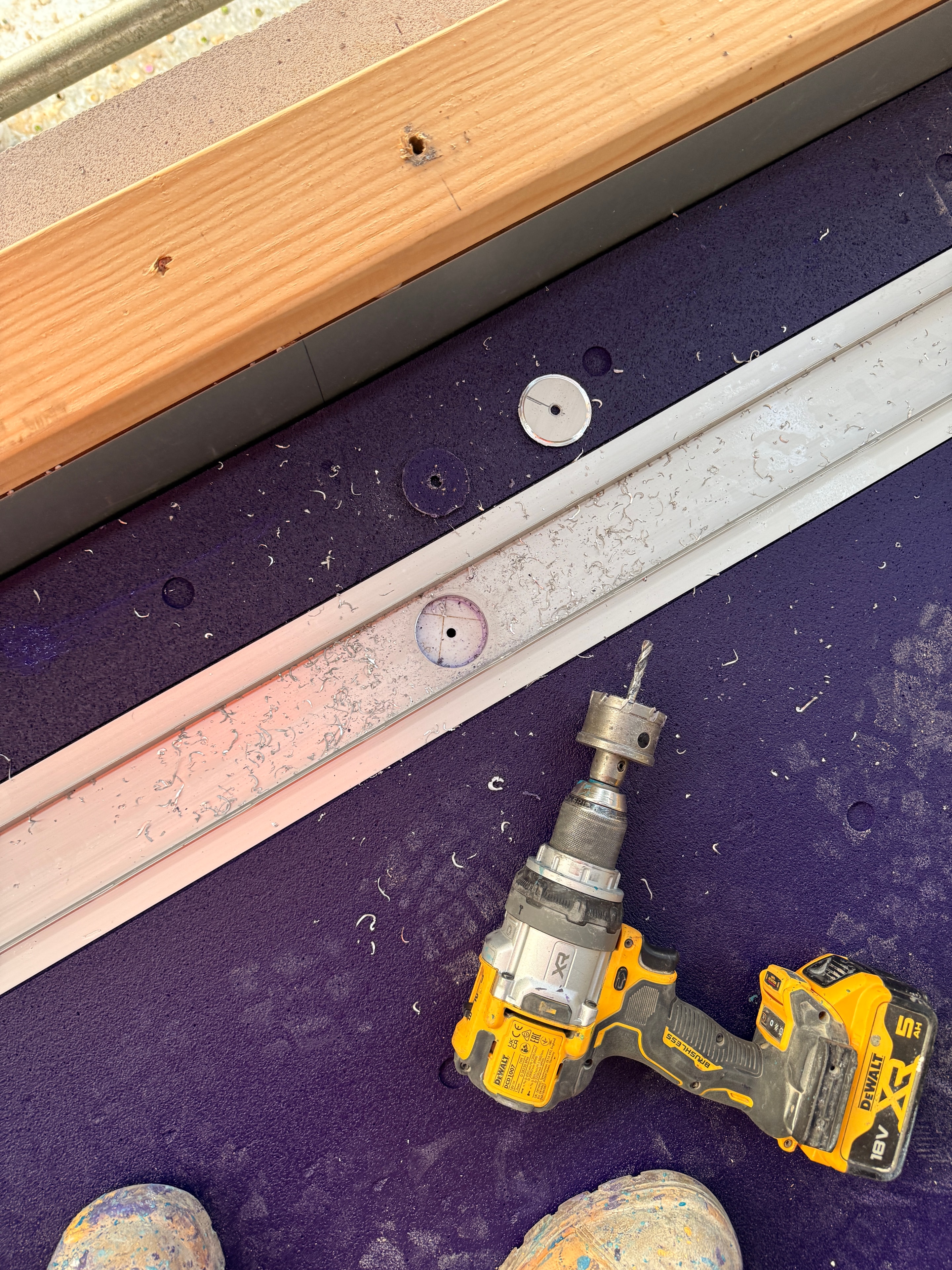 Close-up of DeWalt drill and hole saw cutting drain penetration through purple waterproofing membrane with aluminium threshold track visible — Dandenong balcony by Casey Quality Coatings