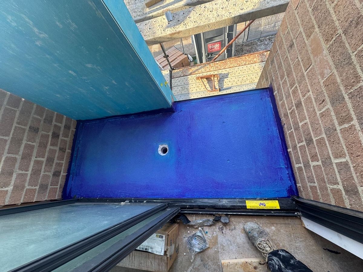 Overhead view of balcony with bright blue waterproofing membrane applied — central floor waste sealed, perimeter upturns done — Rowville new-build by Casey Quality Coatings